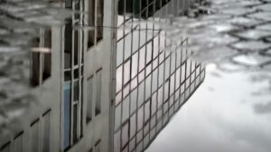 Spiegelung des ehemaligen Flebbe-Haus in einer Regenpfütze am Damm